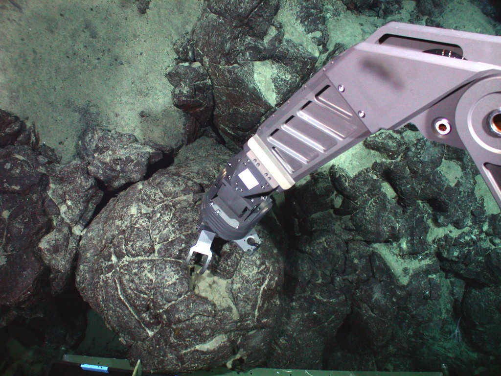 Underwater action scene of robotic mechanical arm on the JASON2 submersible collecting a pillow lava sample from Mauna Loa volcano at 10,000 feet below sea level during a 2002 expedition.  Photo taken by camera on JASON2 (Credit: M. Garcia and J.M. Rhodes)